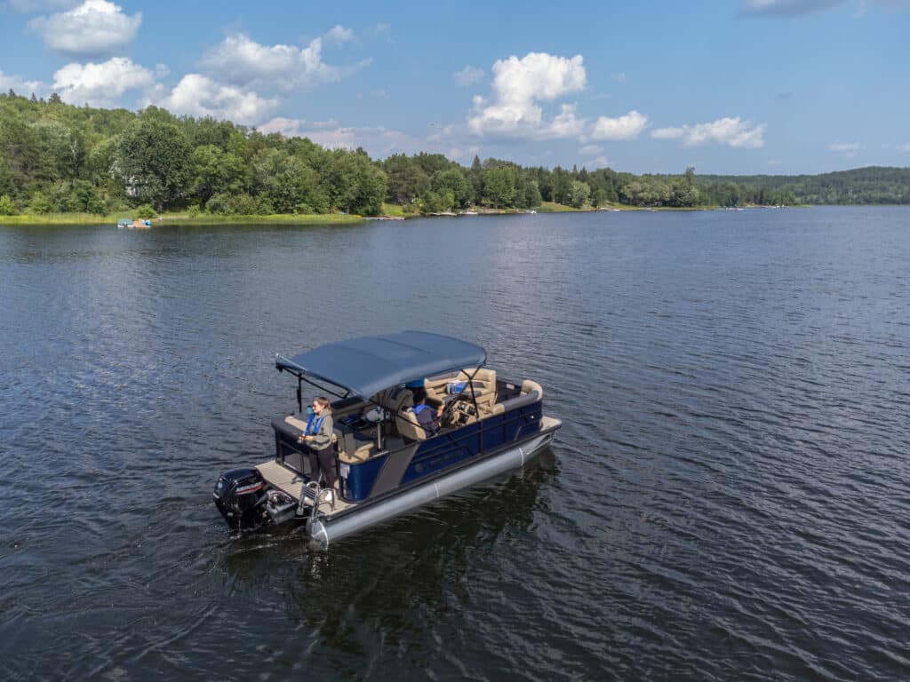 Legend Boats E-Series pontoon boat in the water. There are people fishing off of it.